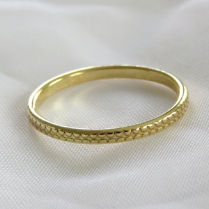 May include: A gold band ring with a textured, patterned surface.