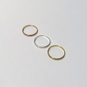 May include: Three simple, thin, braided metal rings in gold, silver, and rose gold.