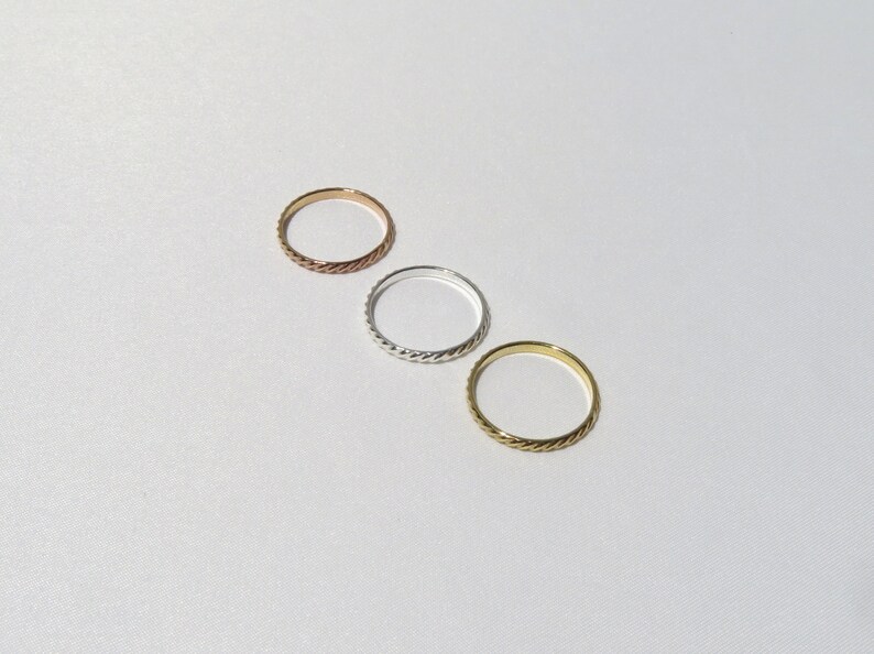 May include: Three simple, thin, braided metal rings in gold, silver, and rose gold.