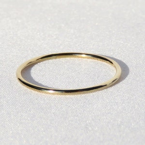 May include: A delicate, thin gold ring. The ring is circular and appears to be made of polished gold. The ring is set against a white, textured background, creating a contrast that highlights its simple elegance. A piece of jewelry.