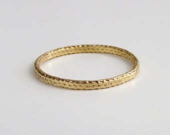 May include: A thin gold band ring with a textured surface.