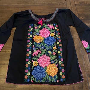Peut inclure: Chemise en coton noir avec des fleurs brod&eacute;es color&eacute;es et une bordure rose. La broderie pr&eacute;sente une vari&eacute;t&eacute; de fleurs, notamment des roses, des lys et des marguerites.