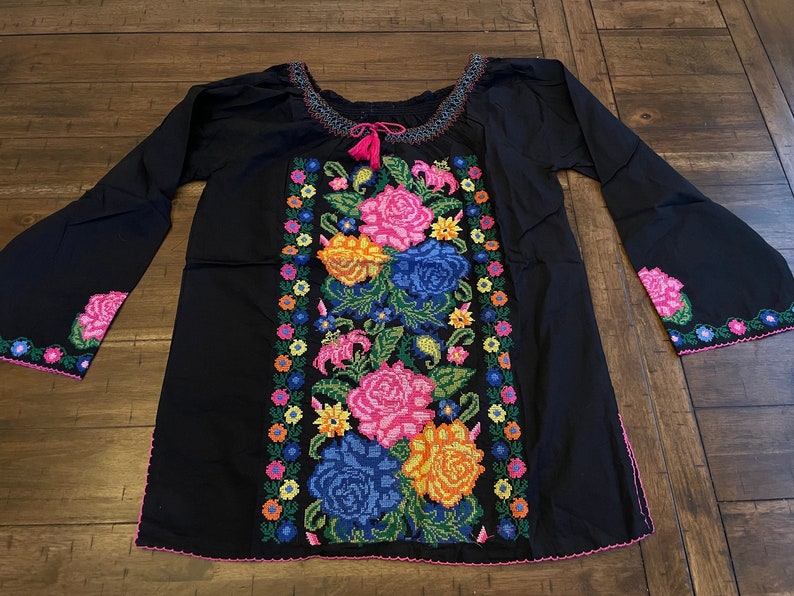 Peut inclure: Chemise en coton noir avec des fleurs brod&eacute;es color&eacute;es et une bordure rose. La broderie pr&eacute;sente une vari&eacute;t&eacute; de fleurs, notamment des roses, des lys et des marguerites.