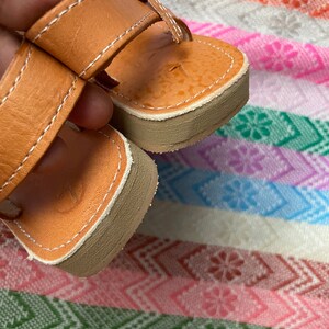 Pu&ograve; includere: Un paio di sandali in pelle marrone con chiusura a fibbia. I sandali hanno un design semplice e sono realizzati in pelle morbida e flessibile.