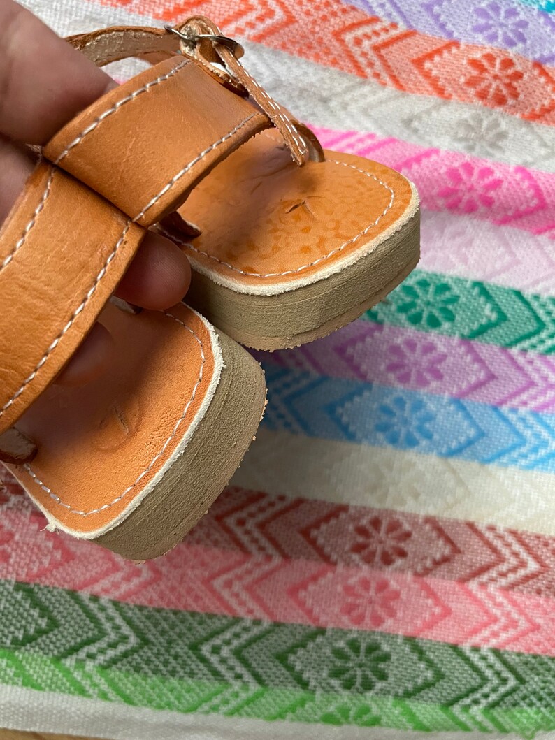 Pu&ograve; includere: Un paio di sandali in pelle marrone con chiusura a fibbia. I sandali hanno un design semplice e sono realizzati in pelle morbida e flessibile.