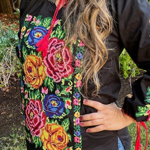 Peut inclure: Chemise noire brod&eacute;e avec des motifs floraux color&eacute;s, avec des glands rouges sur les manches et l'encolure.