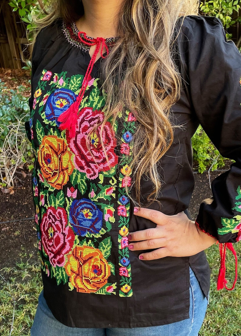 Peut inclure: Chemise noire brod&eacute;e avec des motifs floraux color&eacute;s, avec des glands rouges sur les manches et l'encolure.