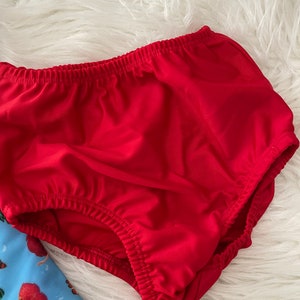 May include: Red cotton diaper with elastic waistband. The diaper is made of a soft, stretchy fabric.