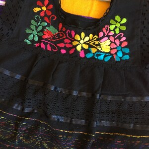 May include: Black embroidered baby dress with colorful floral designs and lace trim.