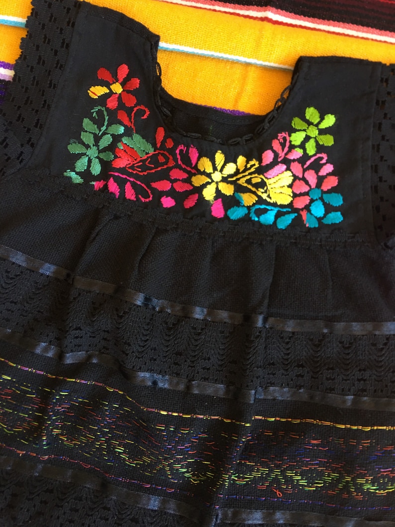 May include: Black embroidered baby dress with colorful floral designs and lace trim.