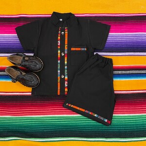 May include: Black short-sleeved shirt with colorful trim and matching black shorts. The shirt has a button-up collar and a pocket on the left side. The shorts have a colorful trim around the waistband and legs.