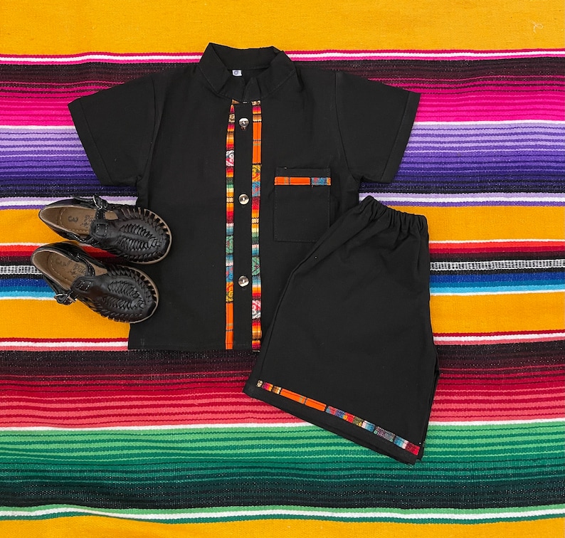 May include: Black short-sleeved shirt with colorful trim and matching black shorts. The shirt has a button-up collar and a pocket on the left side. The shorts have a colorful trim around the waistband and legs.