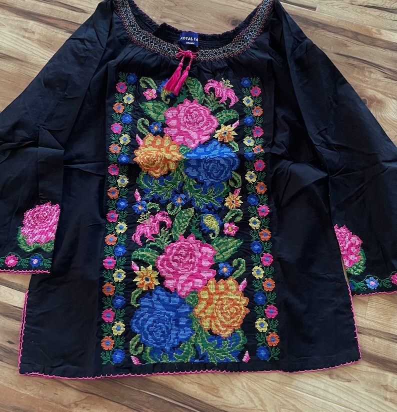 Peut inclure: Chemise noire &agrave; manches longues avec un motif de broderie florale. La broderie pr&eacute;sente des fleurs color&eacute;es, notamment roses, jaunes, oranges, bleues et vertes. La chemise a un col fronc&eacute; et un lien au cou.