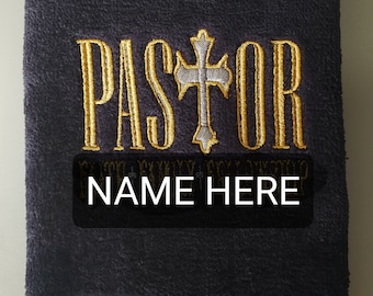 May include: A dark blue towel with a gold embroidered cross and the word "PASTOR" above the text "NAME HERE". The towel has a fringe border.