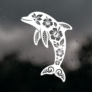 May include: A white vinyl decal of a dolphin silhouette featuring intricate cut-out patterns of hibiscus flowers and tropical leaves. The design is oriented vertically with the dolphin leaping, showcasing detailed floral motifs across its body.
