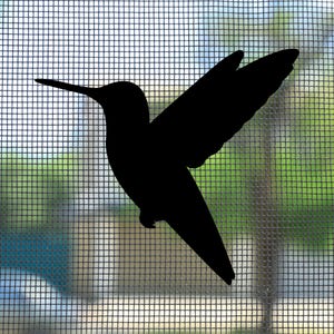 May include: A solid black silhouette of a hummingbird in flight, featuring a long, slender beak, pointed wings extended upwards, and a tapered tail. The bird shape is positioned against a light-coloured, fine-mesh window screen background.