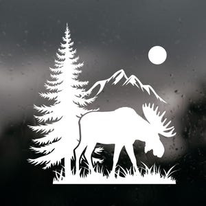 May include: White silhouette of a moose with large antlers, standing in grass, with a pine tree, mountains, and a full moon in the background. The design is a nature-themed graphic.