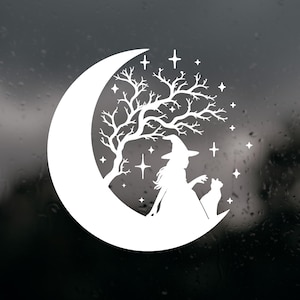 May include: A white vinyl decal featuring a silhouette of a crescent moon, a bare tree with intricate branches, a figure wearing a pointed hat, and a cat sitting together. The design is accented with various four-pointed stars of different sizes.