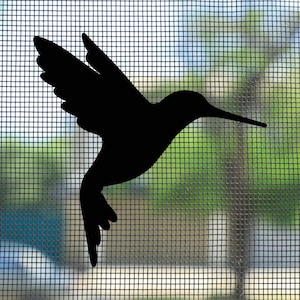 May include: A solid black silhouette of a hummingbird in flight, captured in profile with wings extended upwards and a long, slender beak pointing to the right. The bird shape is displayed against a fine, light-coloured grid screen mesh.