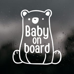 以下が含まれることがあります： 座っているクマのスタイライズされた線画が描かれた白いビニールステッカー。クマには丸い耳、目となる2つの小さな点、小さな鼻があります。クマの胴体部分には「Baby on board」という文字が、すっきりとしたサンセリフ体で印刷されています。
