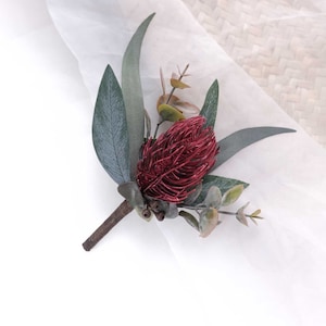 May include: A burgundy red faux flower with green leaves, a popular choice for wedding bouquets and buttonholes.