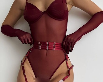 May include: A deep burgundy bodysuit crafted from sheer mesh fabric, featuring thin adjustable shoulder straps and a structured underwire bodice. The set includes matching sheer opera-length gloves and a multi-strap garter belt with metal hardware.