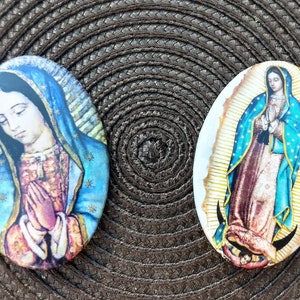 Könnte beinhalten: Zwei ovale religiöse Kunstwerke mit der Jungfrau Maria. Eines zeigt Maria in Blau und Rosa, die Hände zum Gebet gefaltet. Das andere zeigt Maria in einem blauen Umhang mit goldenen Akzenten und einem braunen Gewand.