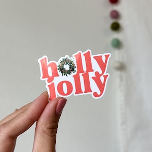 May include: A white sticker with the words "Holly Jolly" in red lettering. A green holly wreath with red berries is in the middle of the word "Jolly".