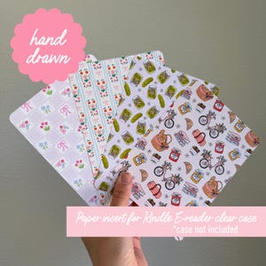 May include: Four decorative paper inserts for a Kindle e-reader clear case, each with a unique pattern. One features a floral and bow design, another has a floral stripe, and the others have food-themed illustrations. The text "hand drawn" and "Paper insert for Kindle E-reader clear case *case not included" are visible.