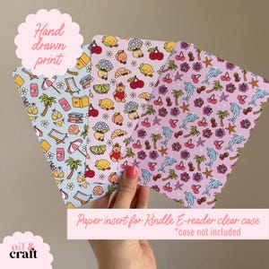May include: Three paper inserts for Kindle e-readers with colorful, hand-drawn patterns. Designs include beach scenes, cartoon characters, and tropical elements. The text "Hand drawn print" and "Paper insert for Kindle E-reader clear case *case not included" are visible.