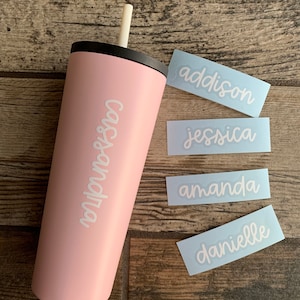 May include: A light pink tumbler with a black lid and a white straw. The tumbler has the name "Cais&Sandra" in white script. Four light blue stickers with names "addison", "jessica", "amanda", and "danielle" are also visible.