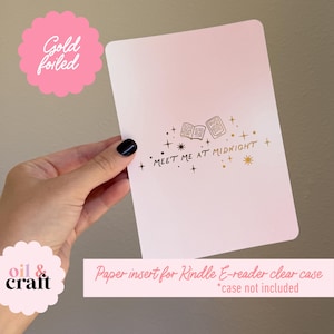 May include: A pink paper insert for a Kindle E-reader clear case. The insert features gold foil text that reads "MEET ME AT MIDNIGHT" with illustrations of books and stars. The words "Gold foiled" are also visible.