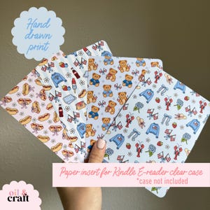 May include: Paper inserts for Kindle e-reader clear cases with hand-drawn prints. The designs feature patterns of teddy bears, hot dogs, flags, and other patriotic and summer-themed illustrations. The text "Hand drawn print" is visible.