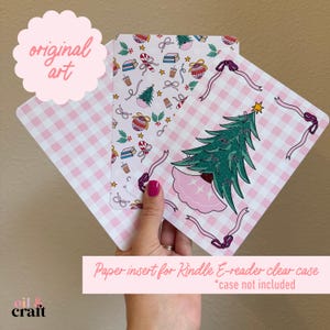 May include: Paper inserts for Kindle e-reader clear cases. The inserts feature a pink and white gingham pattern, Christmas tree, and other holiday-themed illustrations. The text "original art" is visible.