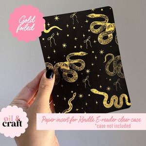 May include: Black paper insert for a Kindle e-reader clear case, featuring gold foil snakes, stars, and bows. The text "Gold foiled" and "oil & craft" are also visible.