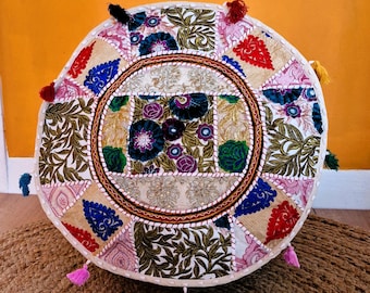 May include: A round, white, embroidered floor cushion with colourful floral patterns and tassels. The cushion is made of patchwork fabric and has a circular design.