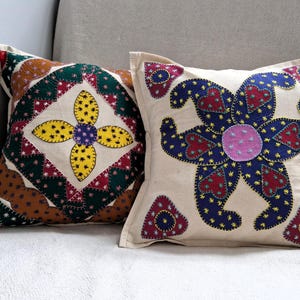 May include: Two decorative throw pillows with floral patterns. One pillow has a yellow, green, and red floral design. The other pillow has a blue, red, and pink floral design.
