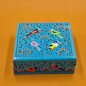 May include: A blue wooden box with a hinged lid. The box is decorated with a colourful floral pattern and five birds. The birds are painted in shades of red, yellow, green, and purple.