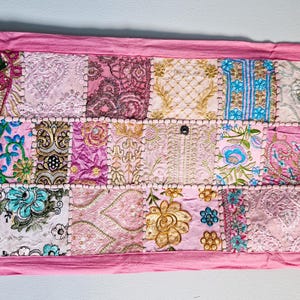 May include: A pink patchwork runner with a variety of floral and geometric patterns in shades of pink, white, and blue.