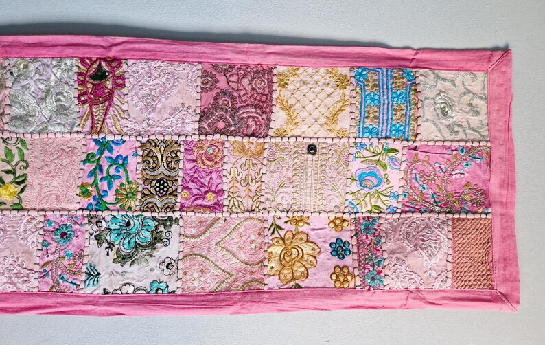 May include: A pink patchwork runner with a variety of floral and geometric patterns in shades of pink, white, and blue.