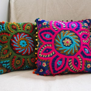 Op de afbeelding: Twee decoratieve kussens met kleurrijke geborduurde bloemenpatronen. De kussens hebben een donkerblauwe, groene en roze achtergrond met gouden, blauwe en rode borduursels. De kussens hebben pompoenen rond de randen.