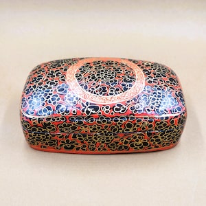 Peut inclure: Une boîte rectangulaire rouge et noire avec un motif floral. La boîte est décorée d'accents dorés et a une bordure noire.