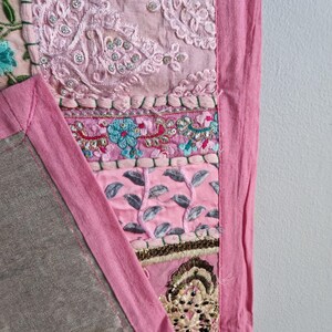 May include: A pink patchwork quilt with a variety of embroidered designs and embellishments. The quilt has a pink border and is made of different fabrics.