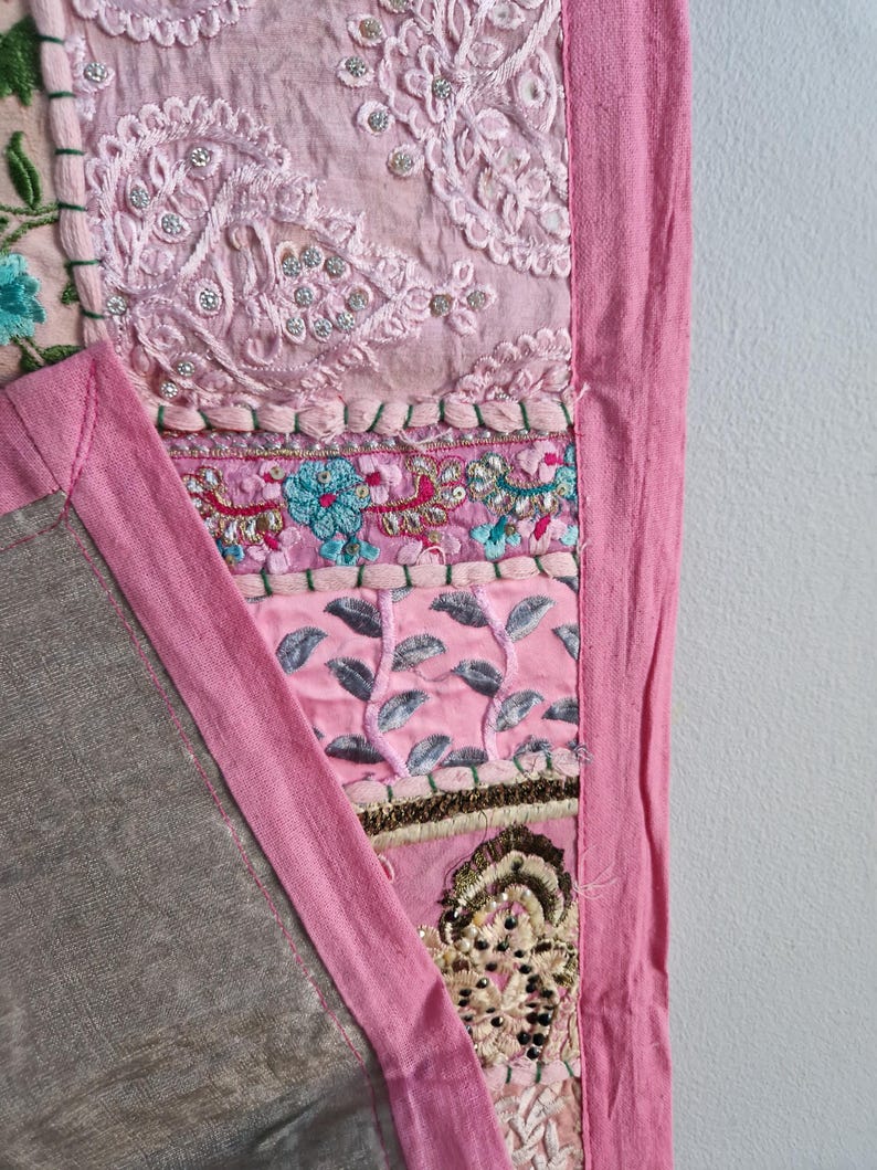 May include: A pink patchwork quilt with a variety of embroidered designs and embellishments. The quilt has a pink border and is made of different fabrics.