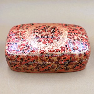 May include: A rectangular box with a floral design in red and gold. The box is made of papier-mâché and has a hinged lid.