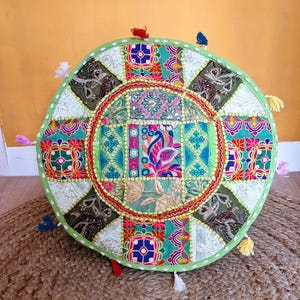 Könnte beinhalten: Ein runder, farbenfroher Bodenkissen mit Patchwork-Design. Das Kissen weist eine Vielzahl von Mustern und Farben auf, darunter Grün, Blau, Rot und Gold. Es ist mit einem grünen Rand und kleinen Quasten versehen.