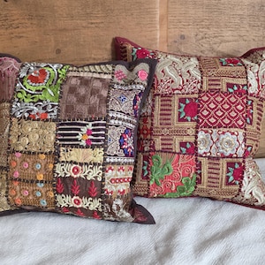 May include: Two decorative throw pillows with patchwork designs. One pillow features a mix of brown, gold, and green embroidered patches. The other pillow has a red and gold embroidered pattern. Both pillows have dark brown borders.