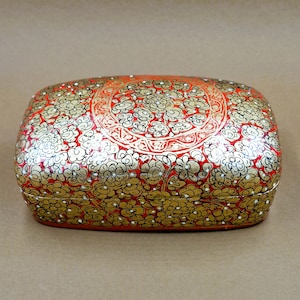 May include: A red and gold rectangular box with intricate floral designs. The box is made of papier-mâché and has a glossy finish.