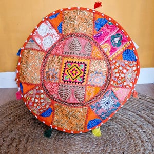 May include: A round, orange, patchwork floor cushion with colorful embroidery and sequins. The cushion has a white trim and tassels.