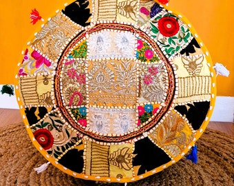 May include: Circular patchwork floor cushion in a variety of colours and patterns. The cushion features gold, black, and yellow fabrics with floral and geometric designs. Tassels are attached to the edges, adding a decorative touch to this bohemian-style home decor item.